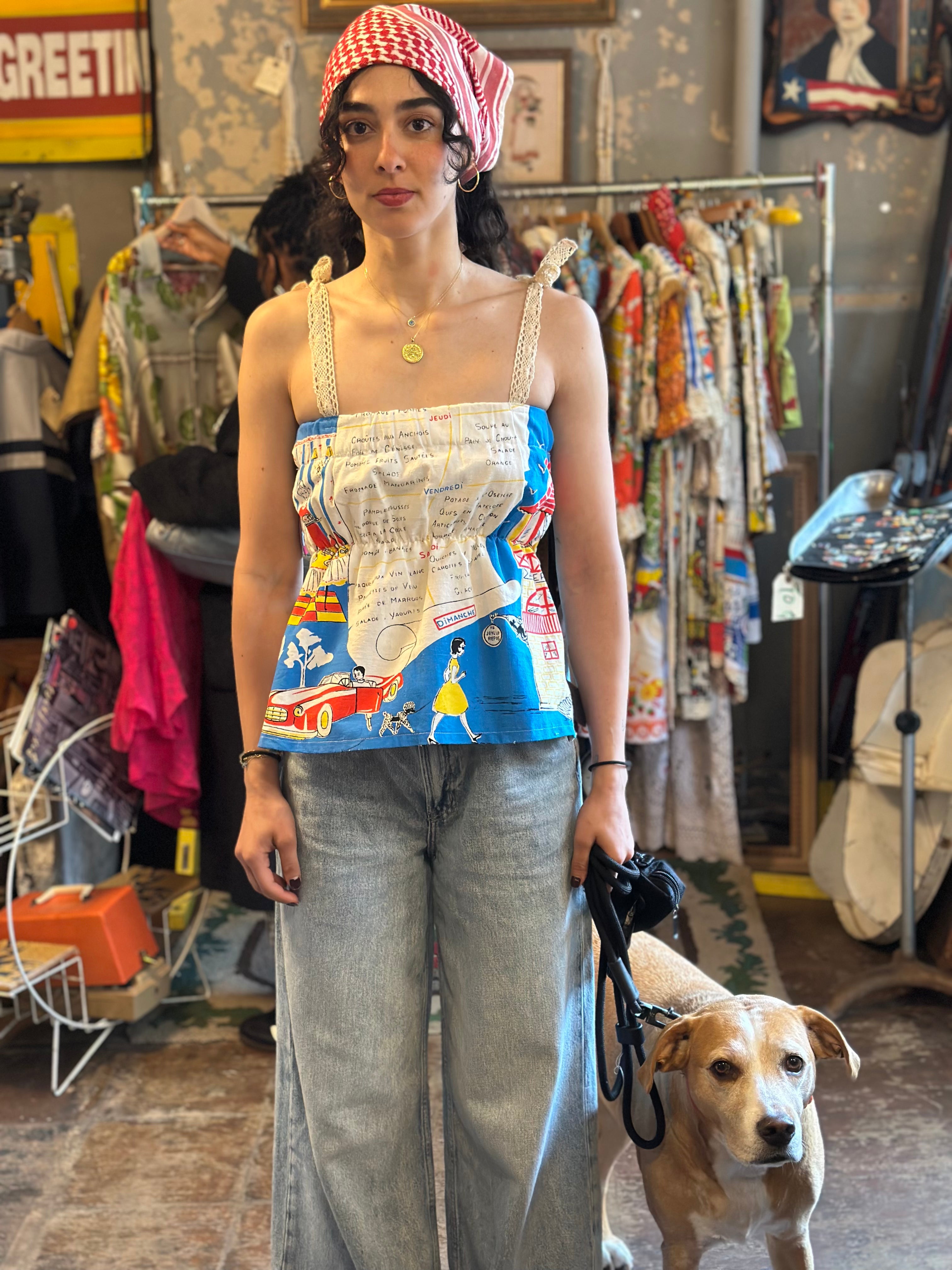 Woman in a colorful top and jeans holding a dog in a vintage store setting