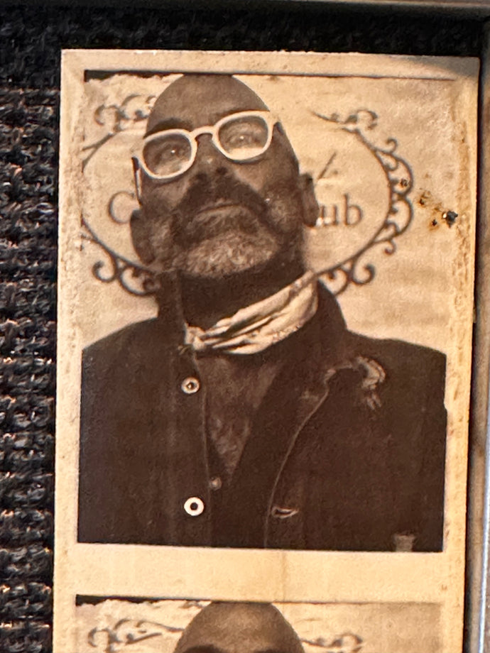Vintage photo of a Joshua, the store owner, wearing glasses and a scarf with decorative elements.