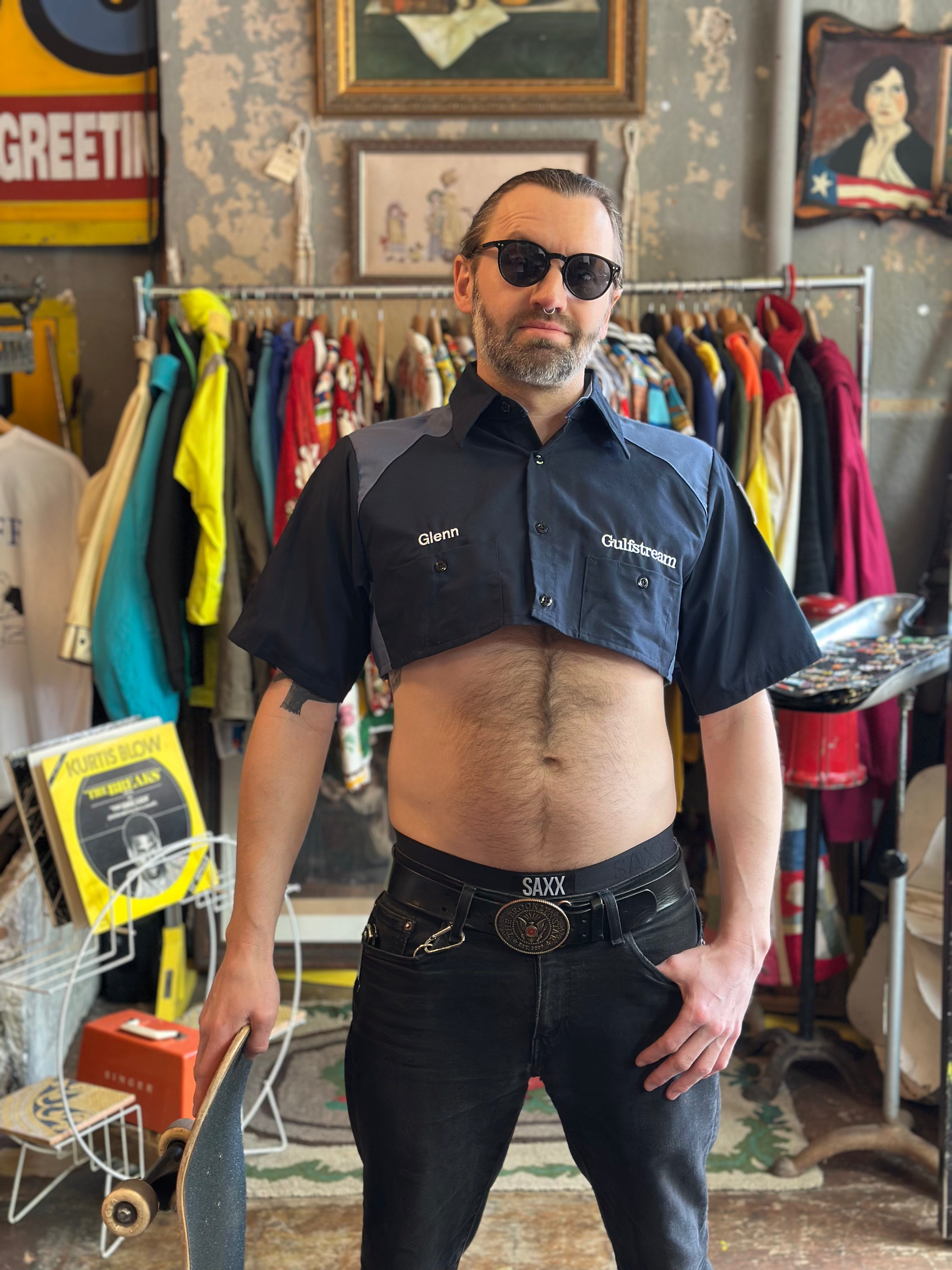 Man wearing a black shirt with 'Glen's Outfitting' logo in a vintage clothing store.