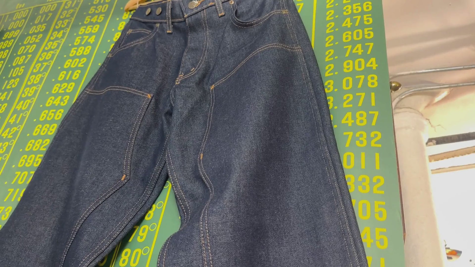 Dark jeans displayed on wall, then video pans to customer browsing through vintage clothing racks